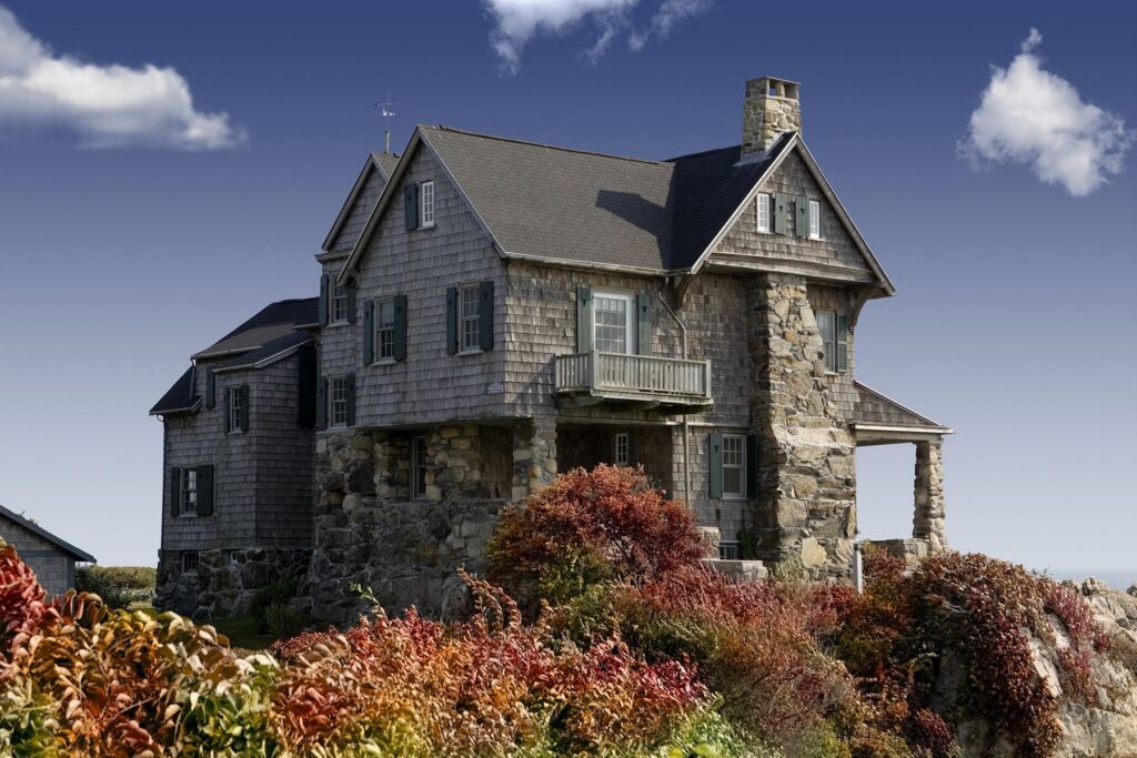 Gray-shingled house with stone details, a chimney, and landscaped grounds