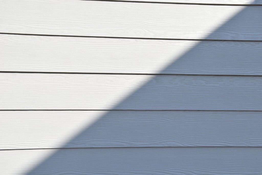 Close-up of light-colored horizontal exterior siding with a diagonal shadow