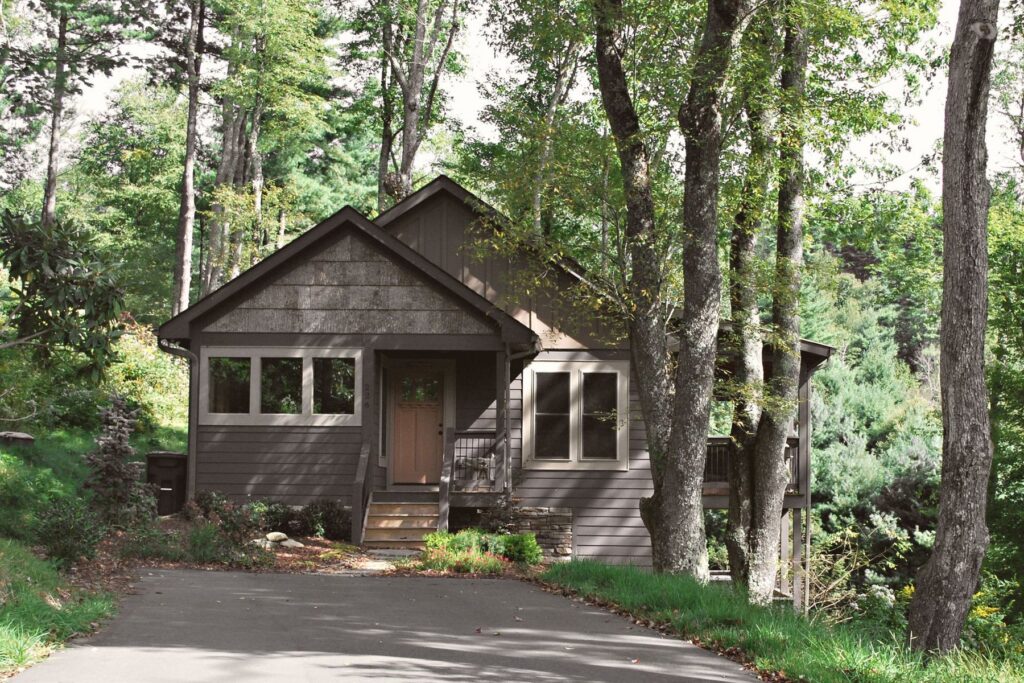 Small dark-sided home surrounded by mature trees and woodland landscaping