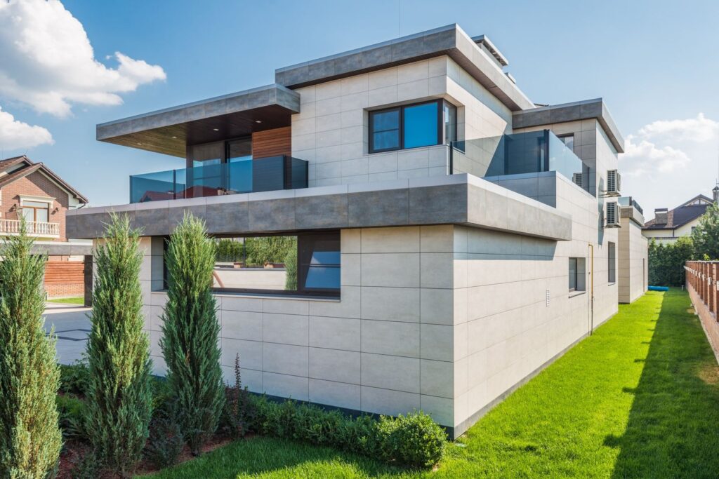 Modern white multi-level house with large windows, a lawn, and a paved walkway
