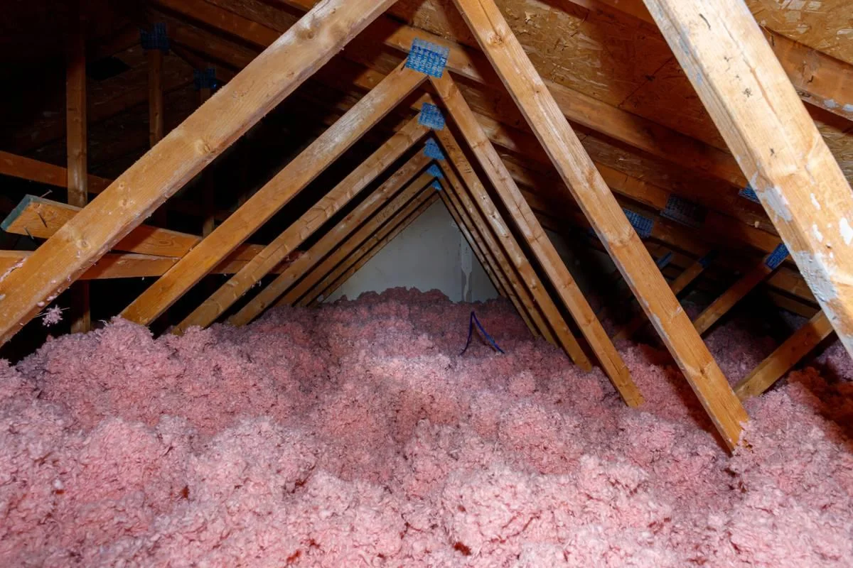 A deep layer of blown-in insulation fills an attic floor up to a small gable window.