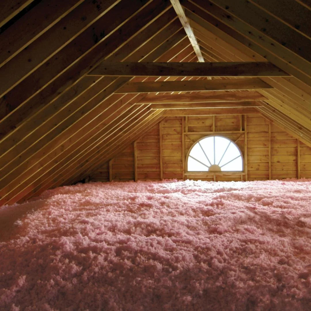 Pink AttiCat blown-in fiberglass insulation spreads evenly across an attic floor beneath the roof rafters.