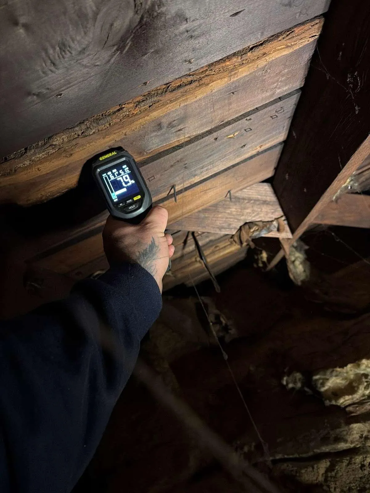 A handheld moisture meter checks a roof rafter for hidden water damage, the kind of hands-on check a camera cannot do.