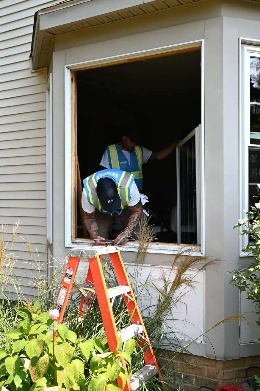 Installers work inside an emptied window opening, setting a replacement unit into the existing frame space.