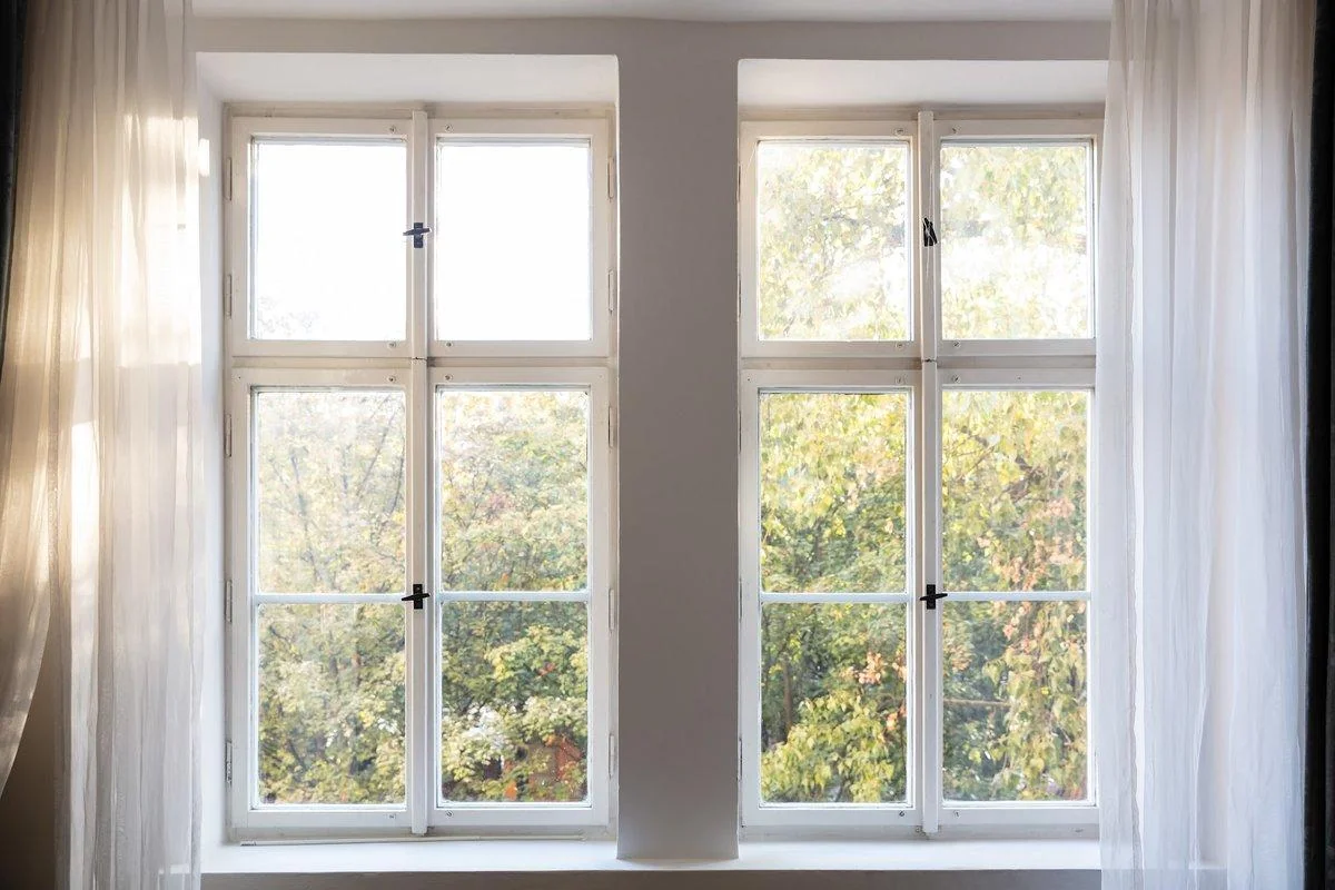 Tall hinged windows that swing open by hand let light into a bright room, the kind of opening a bedroom needs.