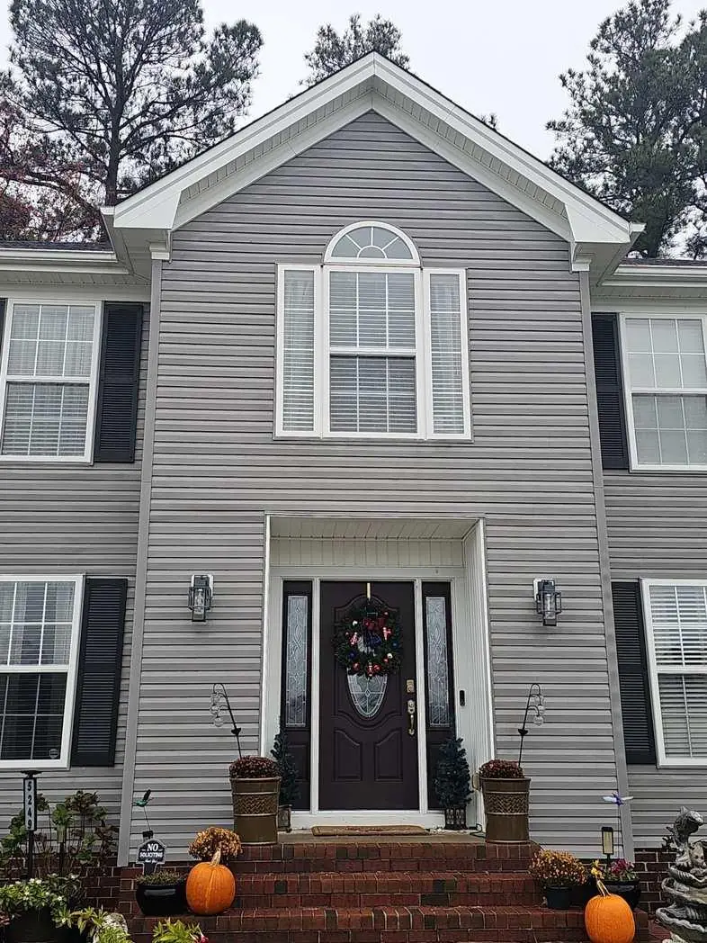 A dark front door with decorative glass sidelights sits at the center of a gray two-story home.