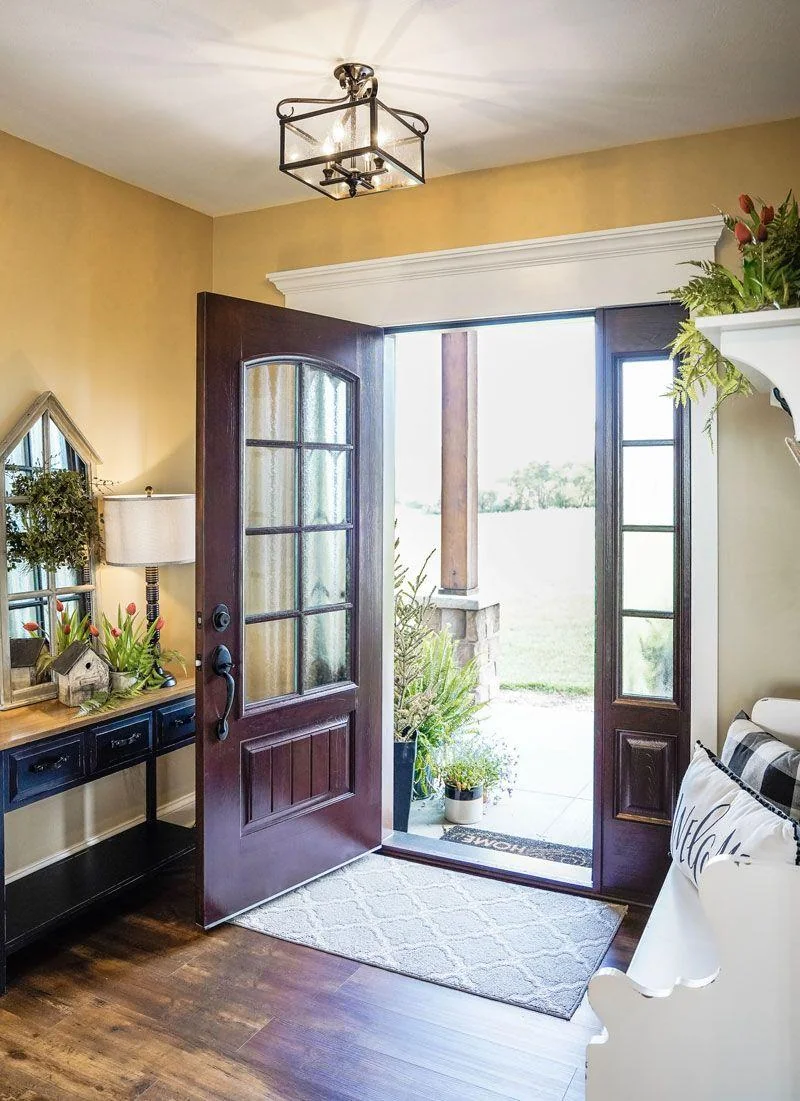 A ProVia Signet fiberglass entry door in a cherry wood-grain finish stands open to a warm-lit entry hall.