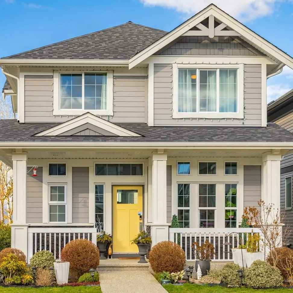 A bright yellow front door draws the eye to the covered porch of a gray two-story home, the curb appeal a new door adds.