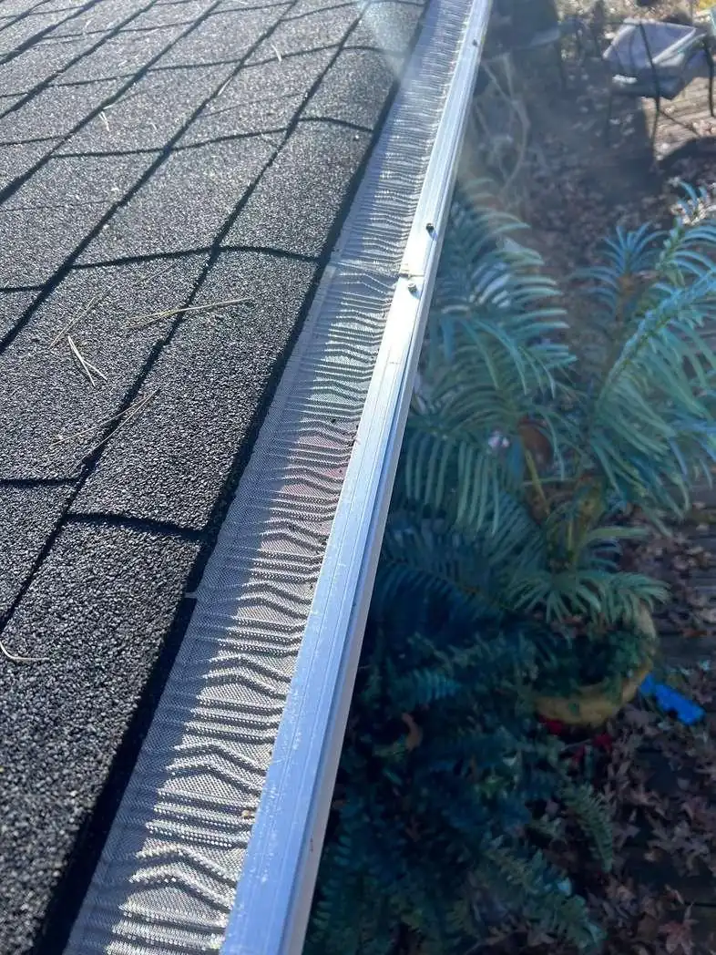 A micro-mesh gutter guard sits fitted over the edge of a dark shingle roof.
