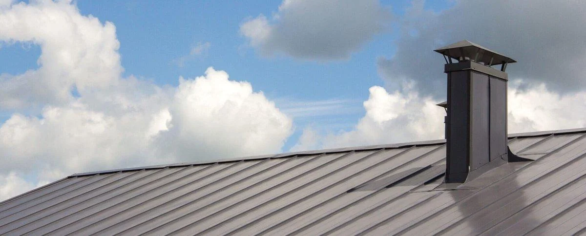 A gray standing-seam metal roof panel rises against a clear sky, its sealed seams built to resist corrosion for decades.