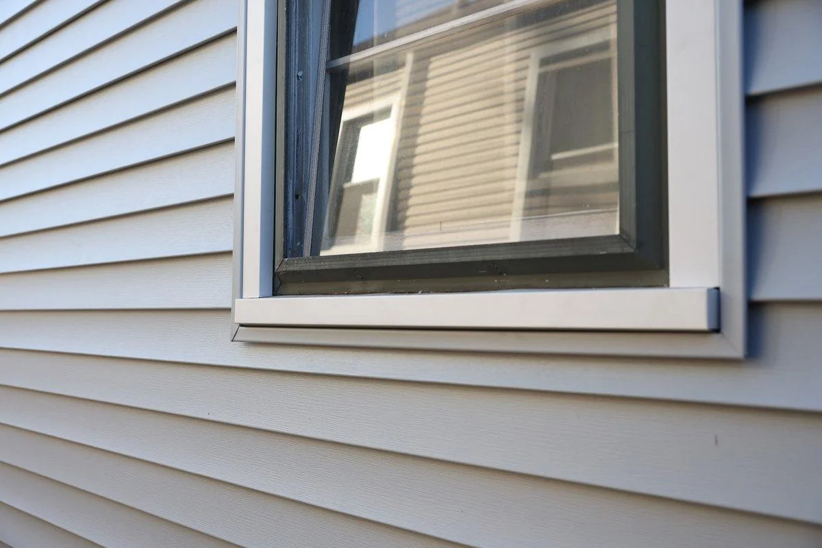 A finished window frame and trim meet blue-gray vinyl siding, the fixed structure that holds the sash in place.