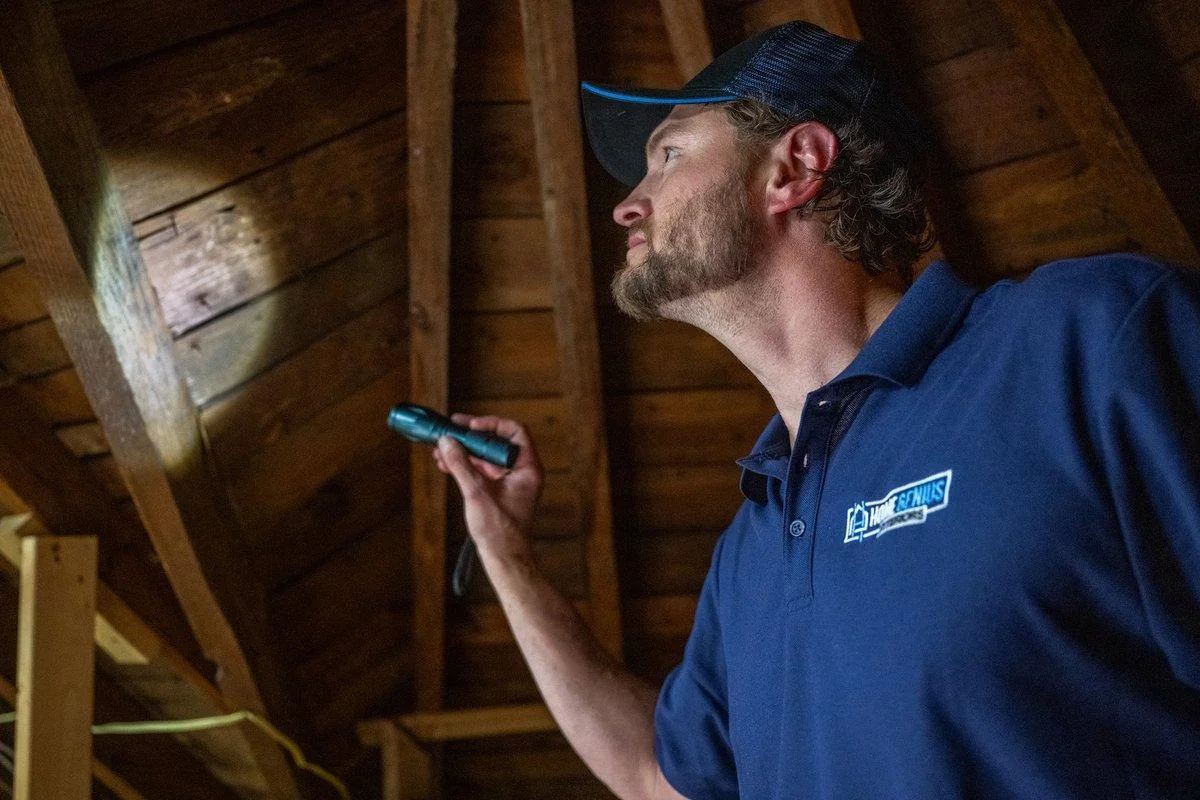 An inspector shines a flashlight on the attic roof decking, checking for the water stains a roof inspection looks for inside.