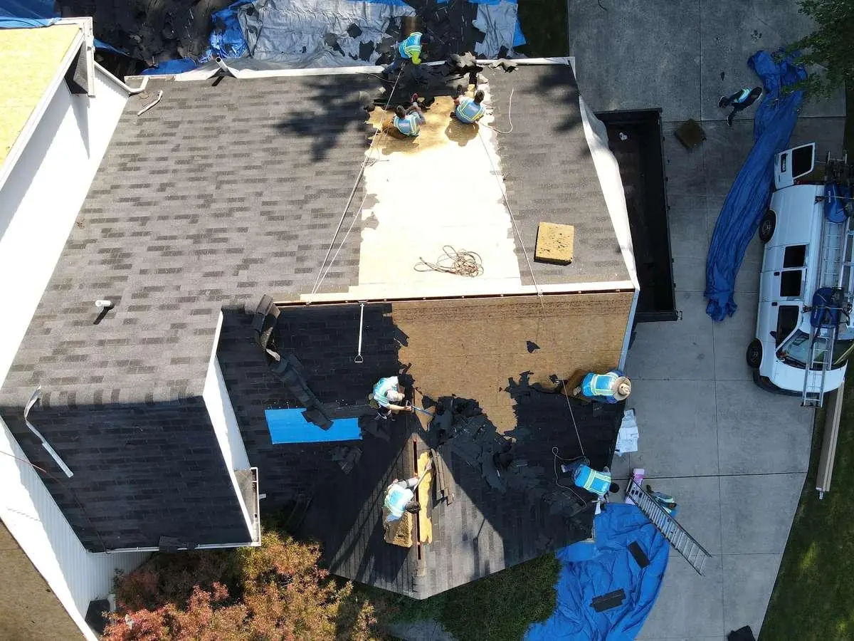 A roof mid tear-off, with old shingles stripped away to expose the bare plywood decking underneath.