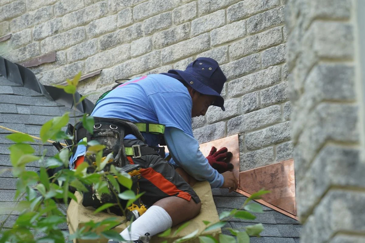 A roofer fits copper flashing where the roof meets a stone wall to keep water out of the joint.