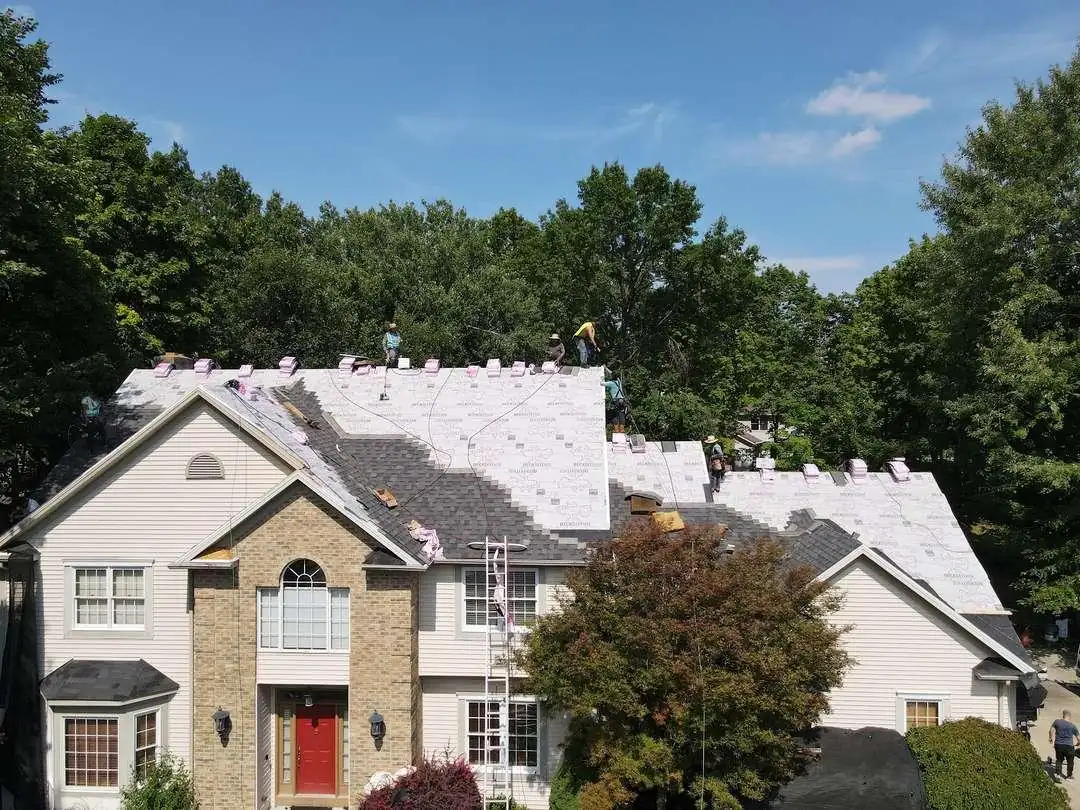 Pink-backed synthetic underlayment covers part of a roof deck while the crew shingles the rest.