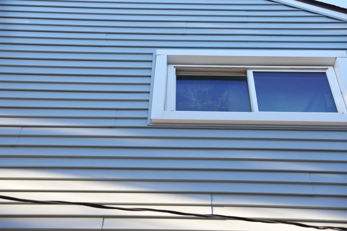 A finished vinyl window frame meets pale blue-gray siding in a clean corner detail, the kind of frame this comparison covers.
