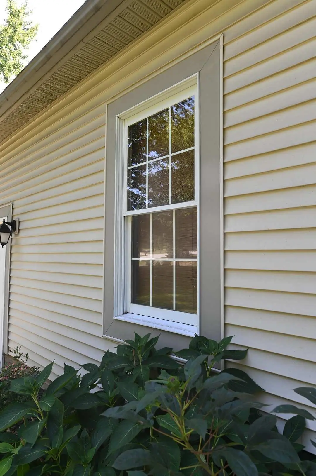 A plain white vinyl double-hung window sits in beige siding, the kind of frame a budget-driven replacement project uses.