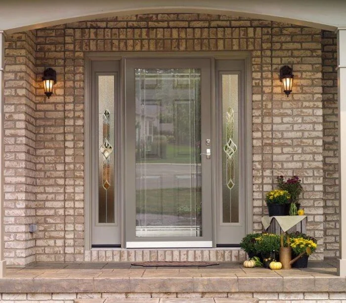 A sandstone full-view storm door with matching sidelites fronts a brick entry, a second door covering the entry door behind it.