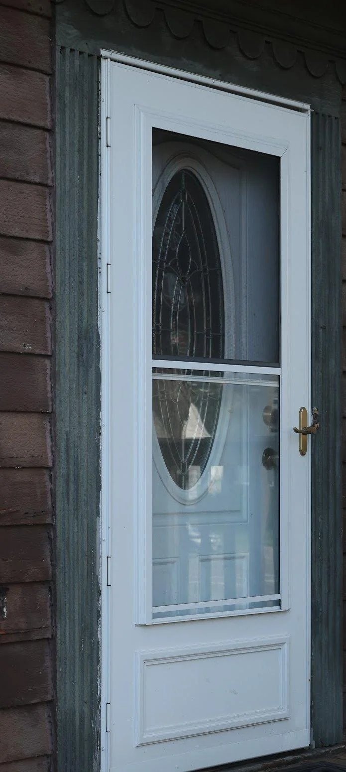 A white storm door with an oval glass lite above a solid kick panel, the mid-view style this section sets against full-view.