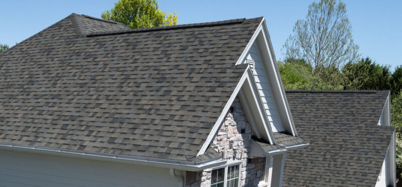 close up of home with stonework siding and grey asphalt shingle roof