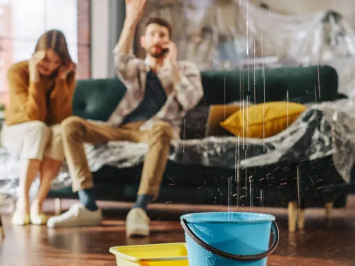 Couple on the phone calling for help while their ceiling leaks during a storm