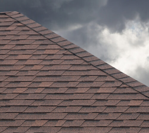An asphalt shingle roof against the backdrop of a stormy sky