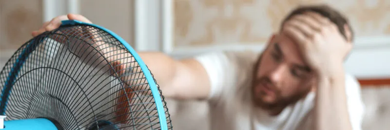 homeowner sitting in front of fan to cool off in hot home