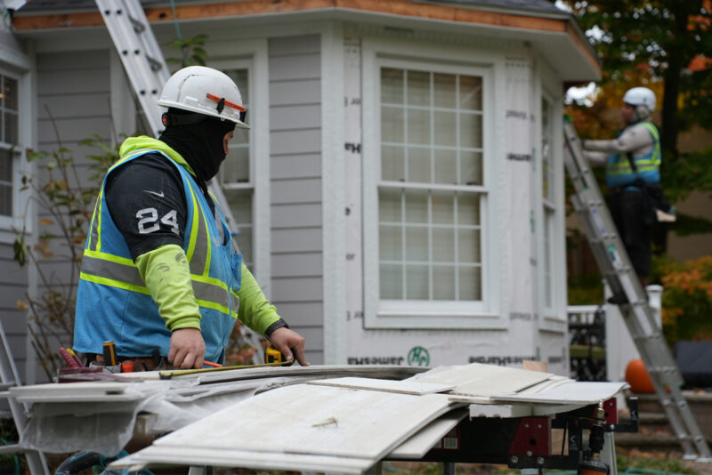 Home Genius Exteriors contractor measuring and cutting siding panels during an installation