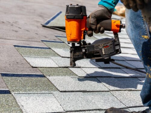 a roofer using a nailgun to replace shingles on a roof