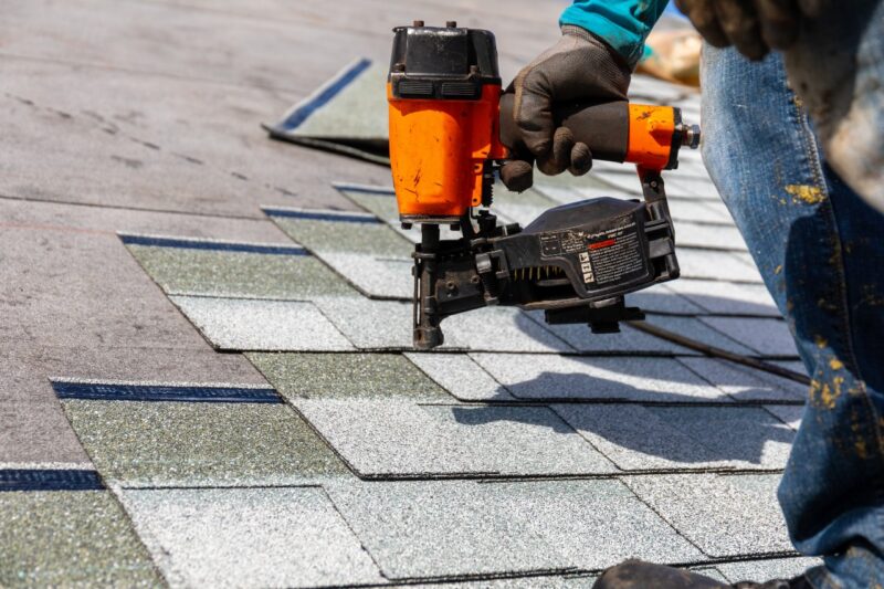 a roofer using a nailgun to replace shingles on a roof