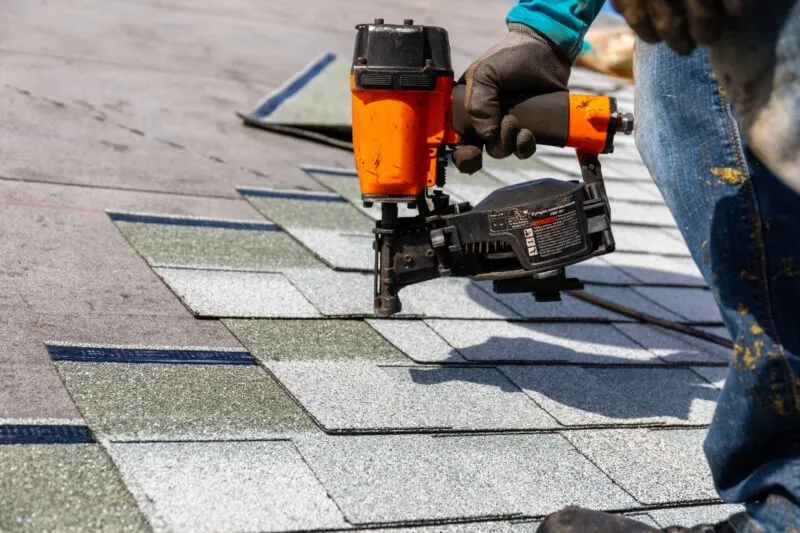 a roofer using a nailgun to replace shingles on a roof